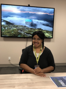 A woman sitting down with arms crossed behind a TV screen